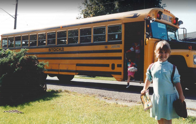 Kate Alatsas as a child, standing by a school bus.